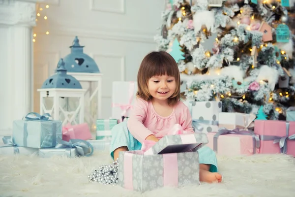 Positieve vrolijke babymeisje zit met de gift van Kerstmis in de buurt van de kerstboom. Gelukkig Nieuwjaar — Stockfoto