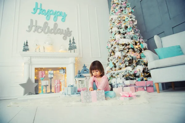 Positive cheerful baby girl sitting with Christmas gift near Christmas tree. Happy New Year — Stock Photo, Image