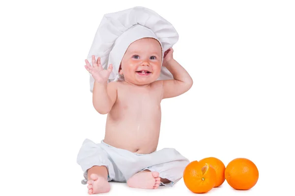 Ett litet barn äter en orange skiva i kocken kostym på vit bakgrund. — Stockfoto