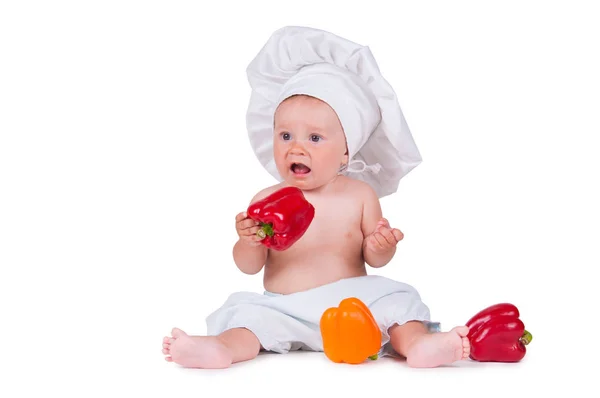 Uma menina engraçada em uma roupa de chefs está comendo pimenta . — Fotografia de Stock