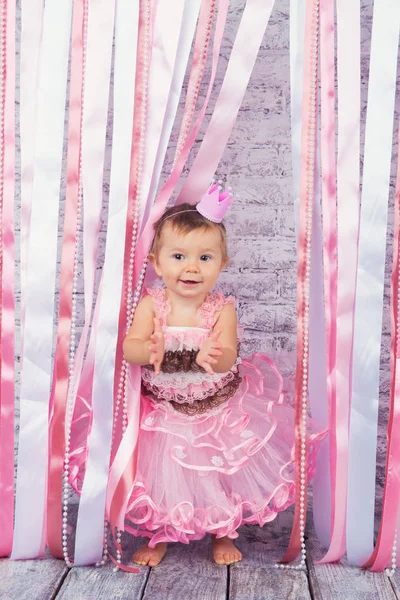 Ein süßes kleines Mädchen in einer Krone und einem wunderschönen rosa Kleid hebt ihre Hände auf der Bühne. — Stockfoto