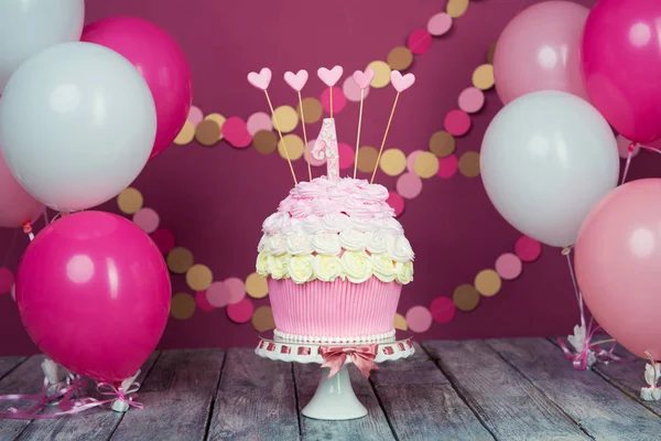 Primeiro bolo de aniversário com uma unidade em um fundo rosa com bolas e guirlanda de papel . — Fotografia de Stock