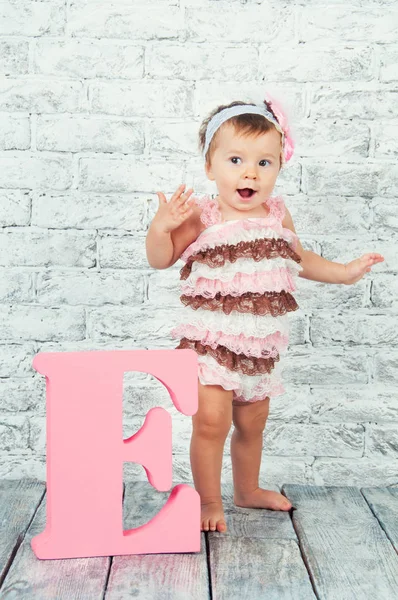 Beautiful and cute girl in pink dress with the letter E. Emotional girl. — Stock Photo, Image