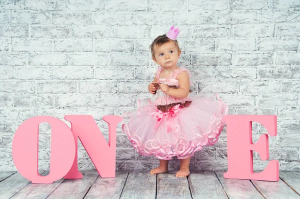 Красива і мила дівчина в рожевій сукні з літерами один на її перший день народження. Емоційна дівчина . — стокове фото