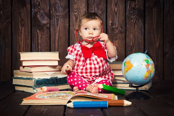 Happy a nice little girl with glasses and pencils against the background of books and a globe — Stock Photo, Image