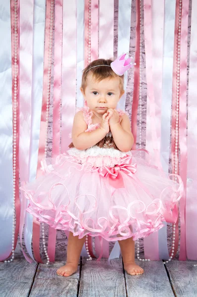 En söt liten flicka i en krona och en vacker rosa klänning höjer händerna på scenen. — Stockfoto