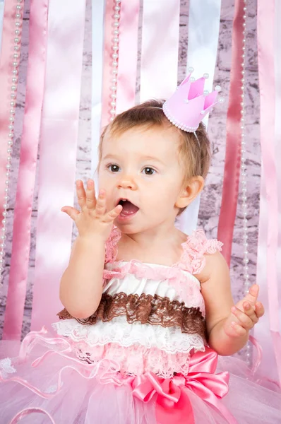 Ein süßes kleines Mädchen in einer Krone und einem wunderschönen rosa Kleid hebt ihre Hände auf der Bühne. — Stockfoto