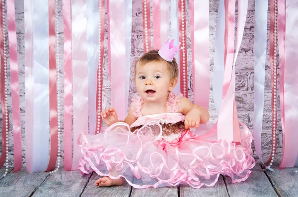 Ein süßes kleines Mädchen in einer Krone und einem wunderschönen rosa Kleid hebt ihre Hände auf der Bühne. — Stockfoto