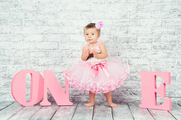 1 歳の誕生日の 1 つ文字とピンクのドレスで美しく、かわいい女の子。感情的な女の子. — ストック写真