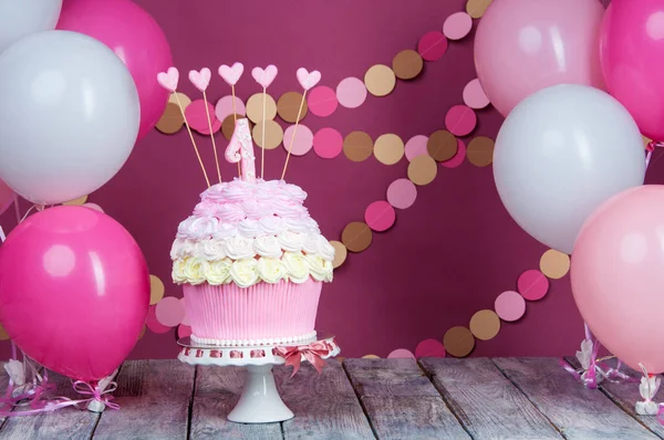 Primeiro bolo de aniversário com uma unidade em um fundo rosa com bolas e guirlanda de papel . — Fotografia de Stock