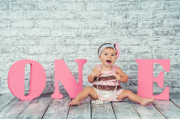 Hermosa y linda chica en un vestido rosa con las letras uno en su primer cumpleaños. Chica emocional . — Foto de Stock
