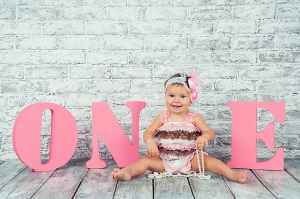 Красива і мила дівчина в рожевій сукні з літерами один на її перший день народження. Емоційна дівчина . — стокове фото