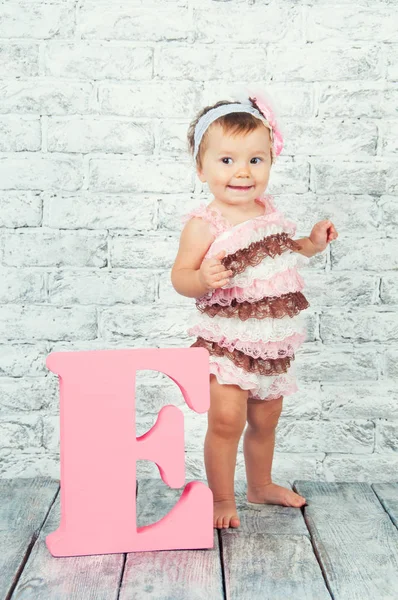 Vacker och söt flicka i rosa klänning med bokstaven E. känslomässiga flicka. — Stockfoto