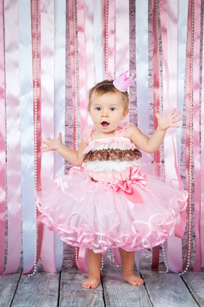 Солодка дівчинка в короні і красива рожева сукня піднімає руки на сцені . — стокове фото
