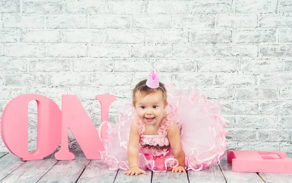Hermosa y linda chica en un vestido rosa con las letras uno en su primer cumpleaños. Chica emocional . —  Fotos de Stock