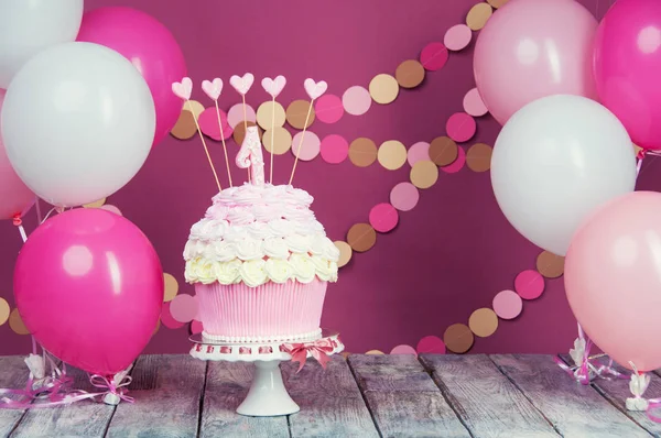 First birthday cake with a unit on a pink background with balls and paper garland.