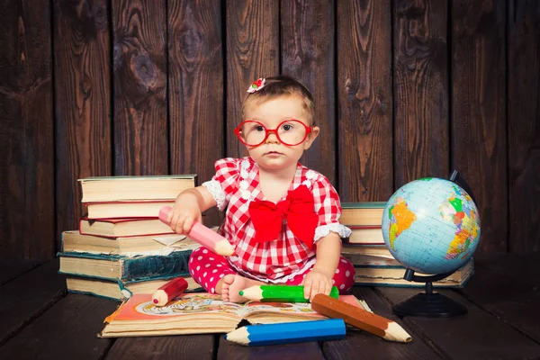 Счастливая маленькая девочка с очками и ручкой на фоне книг и глобуса — стоковое фото