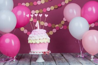 İlk doğum günü pastası ile topları ve kağıt garland pembe bir arka plan üzerinde bir birim.