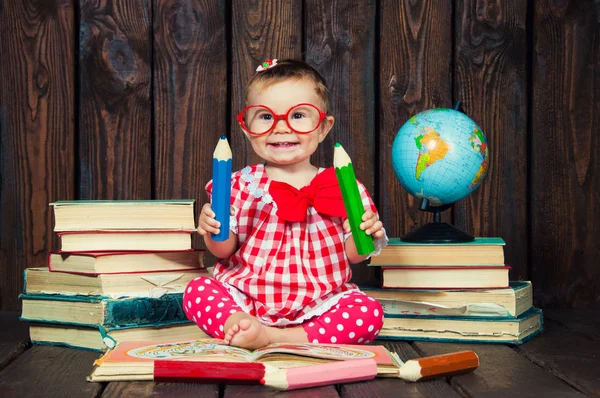 Happy a nice little girl with glasses and pencils against the background of books and a globe — Stock Photo, Image