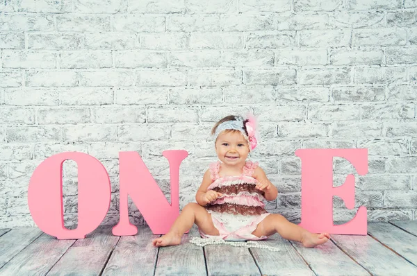 Bella e carina ragazza in un abito rosa con le lettere uno il suo primo compleanno. Ragazza emotiva . — Foto Stock