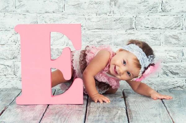 Bella e carina ragazza in abito rosa con la lettera E. Ragazza emotiva . — Foto Stock