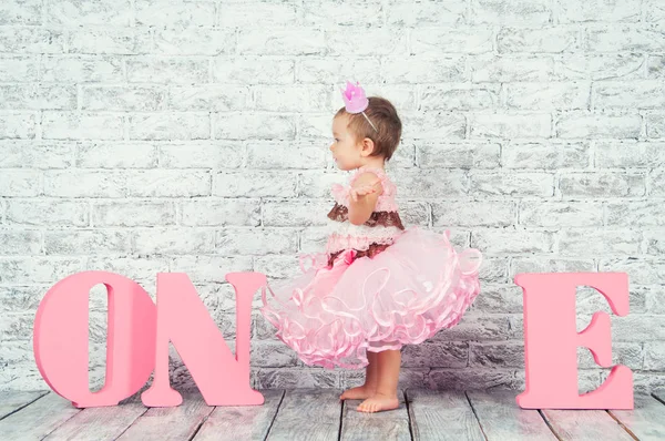İlk doğum gününde harfler bir pembe elbiseli güzel ve şirin kız. Duygusal kız. — Stok fotoğraf
