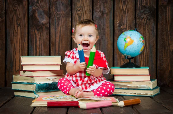 Happy a nice little girl with glasses and pencils against the background of books and a globe — Stock Photo, Image