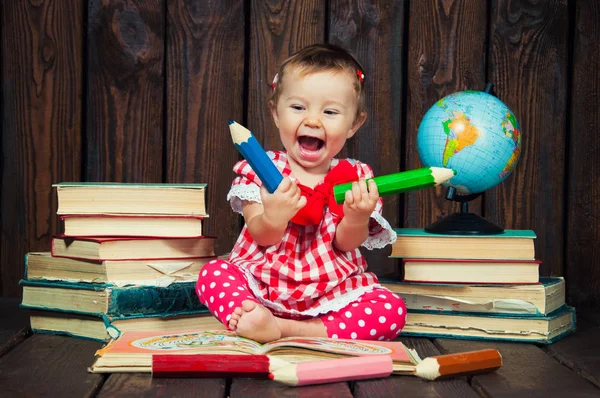 Feliz uma menina agradável com óculos e lápis contra o fundo dos livros e um globo — Fotografia de Stock