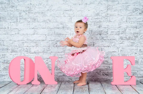 1 歳の誕生日の 1 つ文字とピンクのドレスで美しく、かわいい女の子。感情的な女の子. — ストック写真