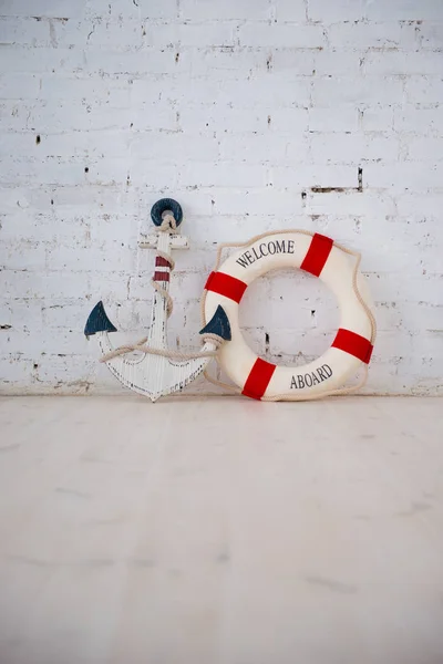 A composition on a sea theme with an anchor and life ring on a white brick wall. — Stock Photo, Image