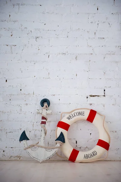 Uma composição sobre um tema do mar com uma âncora e anel de vida em uma parede de tijolo branco . — Fotografia de Stock