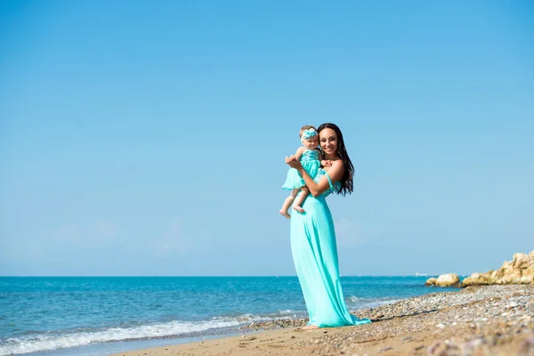 Šťastná rodina v modrých šatech. Matka s dítětem na pláži — Stock fotografie