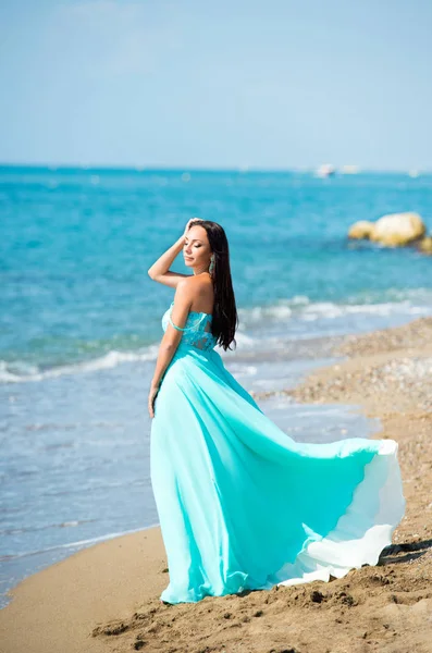 Mujer joven en un vestido azul está caminando por la playa — Foto de Stock