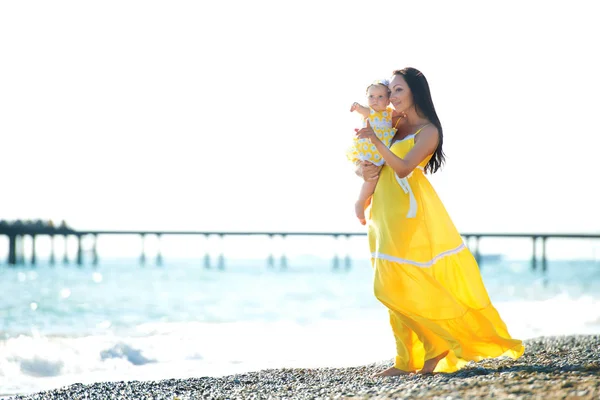 Família feliz em um vestido amarelo. Mãe e filho estão andando na praia — Fotografia de Stock