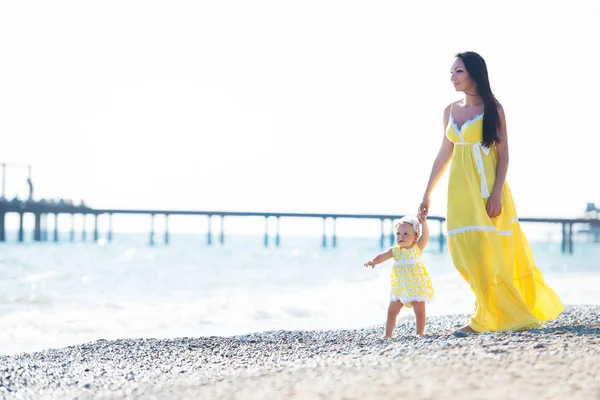 Счастливая семья в жёлтом платье. Мать и ребенок гуляют по пляжу — стоковое фото