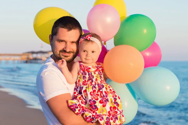 Vater und Tochter mit Luftballons, die tagsüber am Strand spielen. Konzept der freundlichen Familie. — Stockfoto