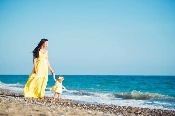 Sarı elbiseli mutlu bir aile. Anne ve çocuk sahilde yürüyor — Stok fotoğraf