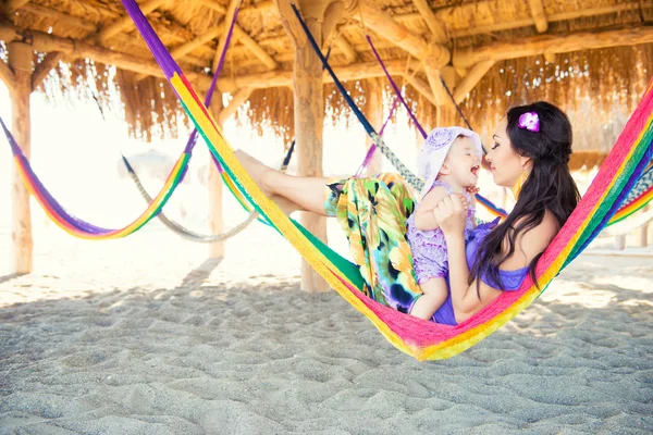 Famiglia elegante felice con la figlia cute che si distende in hammock sulla vacanza di estate nella luce del sole di sera sulla spiaggia. coppia hipster con bambino che riposa e si diverte al tramonto . — Foto Stock