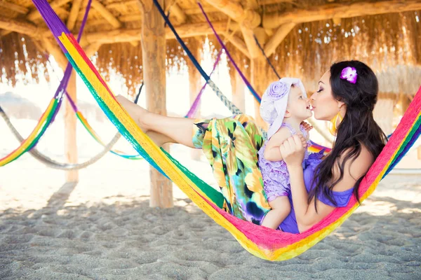 Famiglia elegante felice con la figlia cute che si distende in hammock sulla vacanza di estate nella luce del sole di sera sulla spiaggia. coppia hipster con bambino che riposa e si diverte al tramonto . — Foto Stock