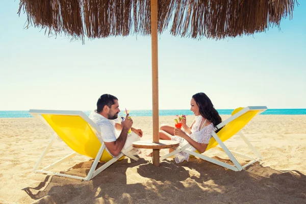 Schattig jong koppel liggend op de ligstoelen op het strand met cocktails — Stockfoto