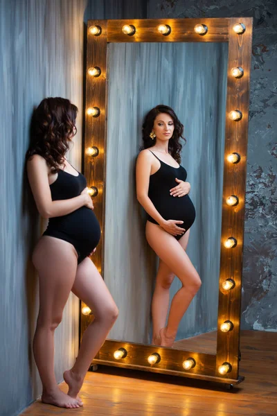 검은 보디 복을 입은 한 젊은 임신부 가등이 달린 아름다운 나무 거울 가까이에 앉아 있다. 내부 석탄층 — 스톡 사진