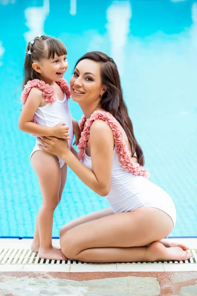 Mãe jovem com a filha bebê nos mesmos trajes de banho brancos sentados na borda da piscina. Roupas para o verão e olhar da família do mar — Fotografia de Stock