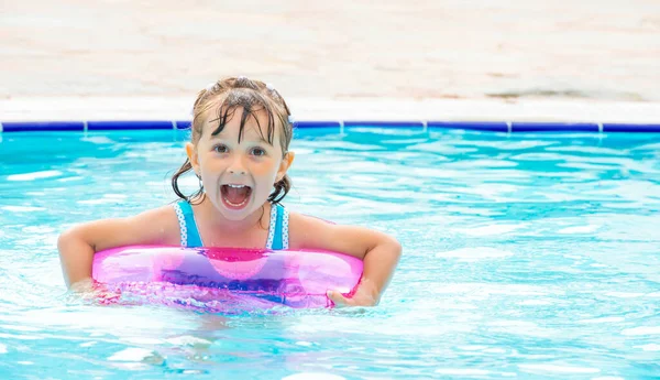 Little girl lying in swimming pool learning to swim on inflatable circle. Summer holidays, heat and water — Stock Photo, Image