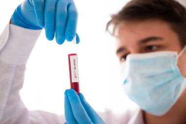 Erkek elinde test tüpü, tıbbi maskeli doktor elinde kırmızı sıvıyla bir şişe tutuyor. Kan örneği kavramı, Covid-19 koronavirüs teşhisi, tıbbi araştırma..