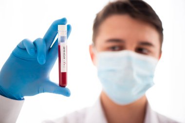 Test tüpü erkek elinde, doktor maskesinde kırmızı sıvıyla bir şişe tutuyor. Kan örneği kavramı, koronavirüs teşhisi, tıbbi araştırma.