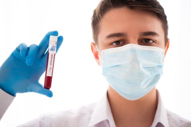 Test tüpü erkek elinde, doktor maskesinde kırmızı sıvıyla bir şişe tutuyor. Kan örneği kavramı, koronavirüs teşhisi, tıbbi araştırma.