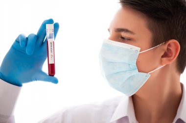 Test tüpü erkek elinde, doktor maskesinde kırmızı sıvıyla bir şişe tutuyor. Kan örneği kavramı, koronavirüs teşhisi, tıbbi araştırma.