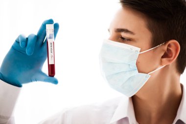 Test tüpü erkek elinde, doktor maskesinde kırmızı sıvıyla bir şişe tutuyor. Kan örneği kavramı, koronavirüs teşhisi, tıbbi araştırma.