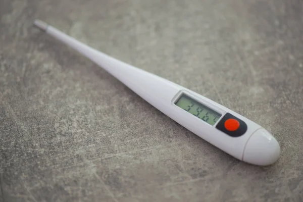 Close-up electronic thermometer for measuring body temperature on a gray background.