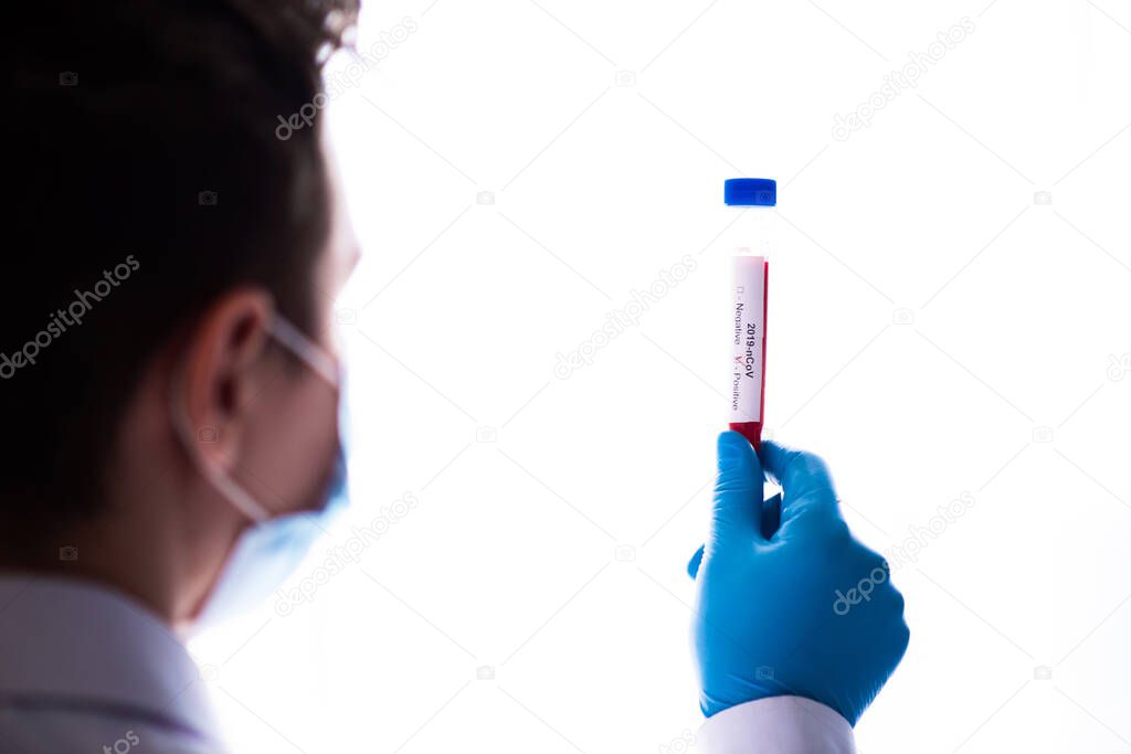 Test tube in male hand close up, doctor in medical mask holding a vial with red liquid. Concept of blood sample, coronavirus diagnostic, medical research.
